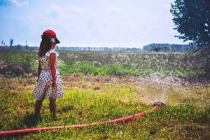 girl on green grass near red hose while pumping water during daytime
