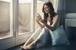 woman sitting beside window at home holding phone