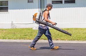 man in white tank top and blue denim pants with leaf blower outdoors during daytime
