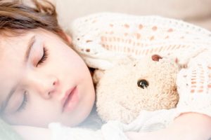 girl sleeping with her brown plush toy in guest bedroom